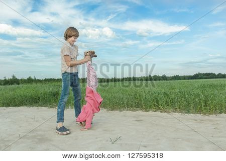 Sibling brother is supporting his younger sister doing handstand on farm field dirt road