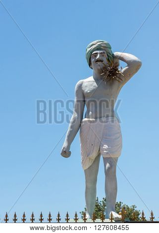 Thanjavur India - October 14 2013: Statue of the common laborer the mustached man who works in the rice fields. Whitish man against blue sky. Wears a green turban a dhoti and has fake straw on shoulder.