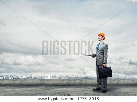 Young handsome man architect in hardhat with project in hand