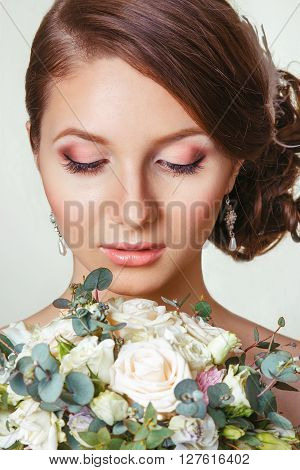 portrait of the beautiful young girl in an image of the bride with ornament in hair.beautiful bride with bouquet looking down. Close-up