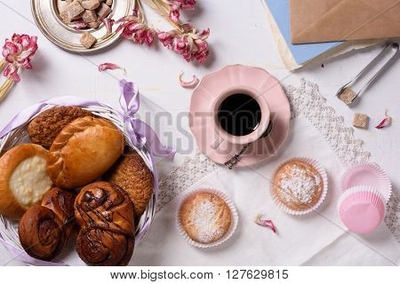 Fresh pastry with coffee, cupcakes, pink tulip flowers over rustic white background. Top view, morning light.