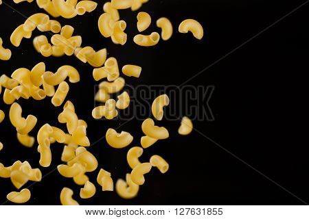 Falling gobetti pasta. Flying yellow raw macaroni over black background. Shallow dof.