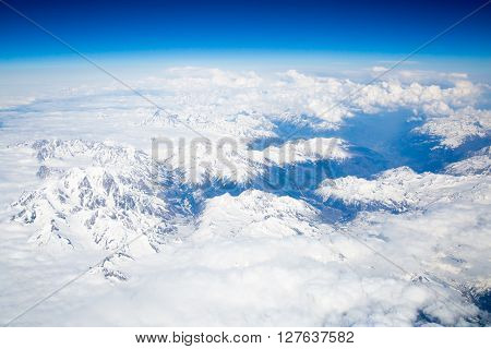 Snow covered mountains and rocky peaks in the French Alps, over blue sky. View from airplane