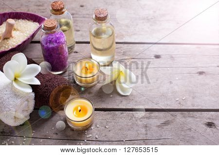 Wellness or spa setting. Bottles with aroma oil sea salt towels and white plumeria flowers in ray of light on vintage wooden background. Selective focus. Place for text.