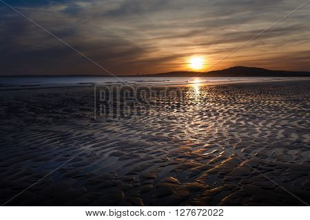 Sunset at Aberavon beach on an outgoing tide with Swansea on the horizon
