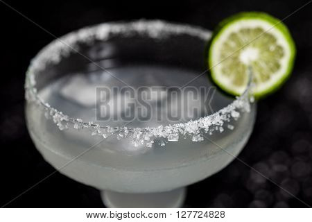 Mexican Margarita cocktail macro photo. Focus on salt on side of glass. Black bacground with sea salt spots on it