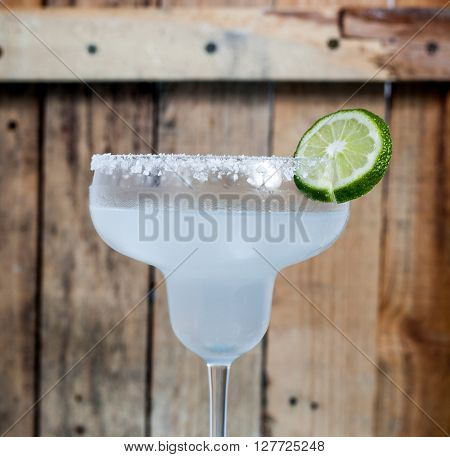 Classic Mexican Cocktail - Margarita in glass with cocktail tubes. Ingredients of cocktail - lime juice, ice, tequila, salt and orange liqueur. Rustic wood bacgkround.