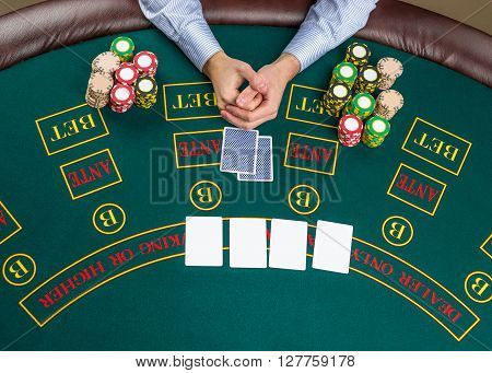 Close up of poker player with playing cards and chips at green casino table, view from above.