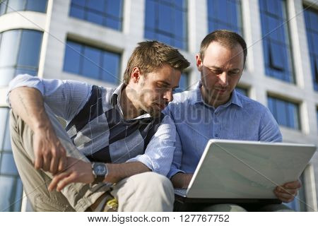 Two young students workong together outside with laptop