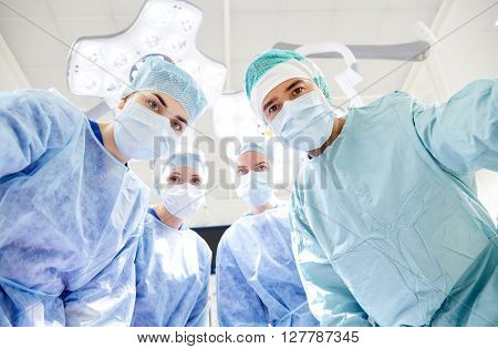 surgery, medicine and people concept - group of surgeons in operating room at hospital looking into camera