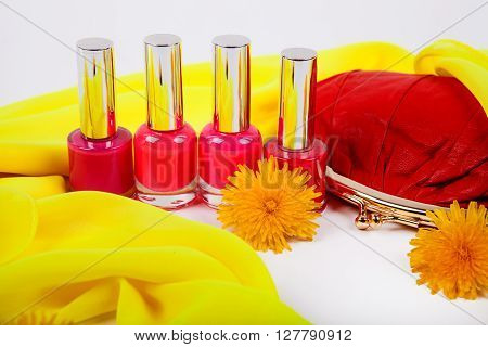 Four red bottle with nail polish and red women's purse on a background of yellow fabric