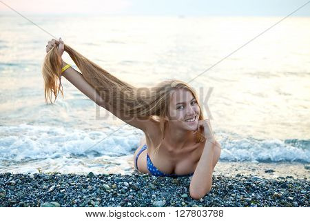 Young beautiful girl in a bathing suit lying on the beach and holding her long beautiful hair on vacation