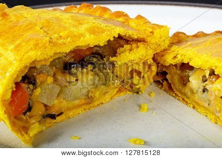 Vegetarian pasty cut in half filled with cheddar cheese onion carrot swede potato and sweet potato in an all butter pastry flavoured with turmeric.