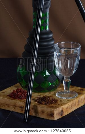 still life of a hookah and a glass of water. neatly laid out on a wooden stand with tobacco .