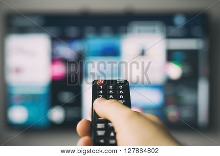 Male hand holding TV remote control against SmartTV operating system