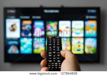 Male hand holding TV remote control against SmartTV operating system