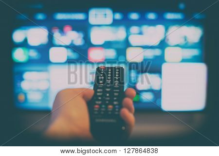 Male hand holding TV remote control against SmartTV operating system