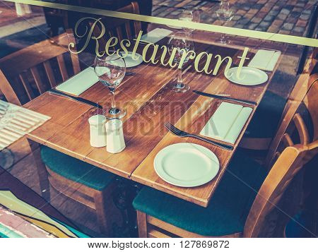 Retro Style Street Image Of A Rustic Restaurant Table Through A Window On A Cobblestone Street In Europe