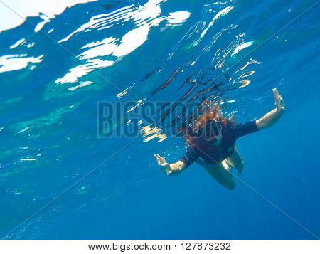 A woman underwater in black swimsuit and mask, loose hair girl snorkeling in mask, red hair young girl diving, girl snorkel in blue sea, tropical sea vacation holiday summer activity, girl on vacation