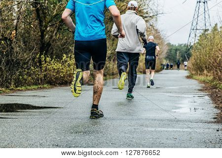 group of runners men running down road in Park. feet in mud