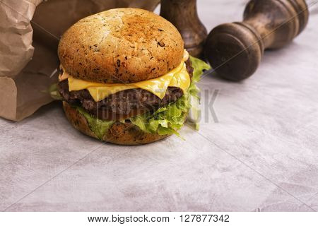 Single beef cheeseburger with vegetables on stone table, selective focus