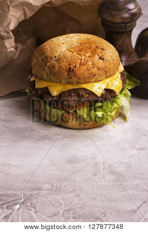 Single beef cheeseburger with vegetables on stone table, selective focus