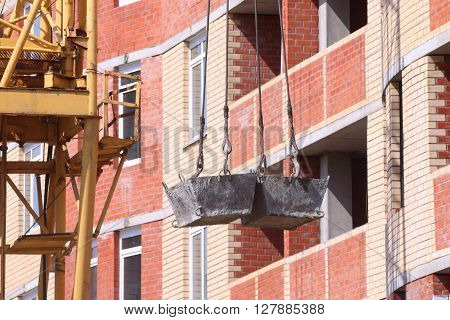 High residential building and hooks of crane lifting concrete solution on floor at construction site