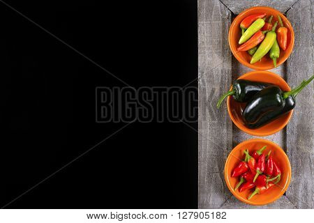 Mexican hot chili peppers colorful mix jalapeno on orange bowls and black background