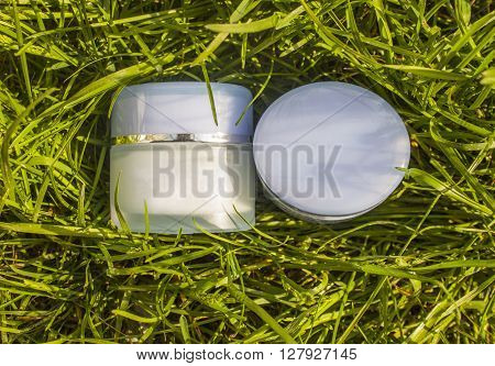 Jar with a cream on a background of green grass. Natural cosmetic.
