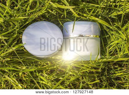 Jar with a cream on a background of green grass. Natural cosmetic.