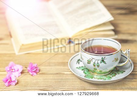 Tea cup the book and flowers on the wooden table. Image with light effects toning. Shallow DOF
