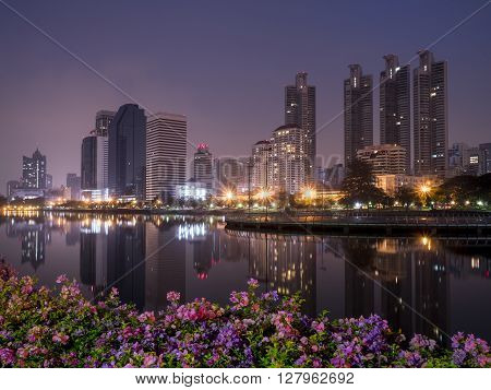 Night light with modern building and flower foreground in the park beside lake at Bangkok Thailand (Benchakitti Park)