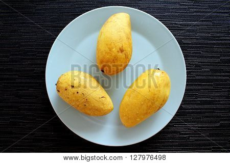 Yellow mango tropical fruit in a mint plate on the black background, exotic fruit flat photo, fresh mango flat picture, mango fruit breakfast view from above, flat shooting of yellow mango on blue