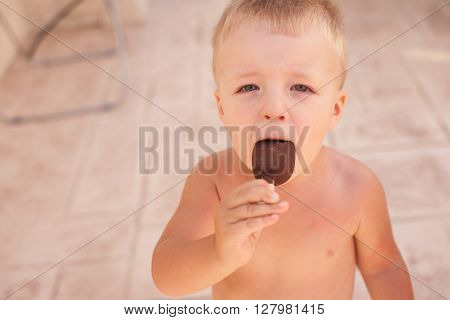 Small sunburnt boy eating ice-cream outdoor in hor summer day