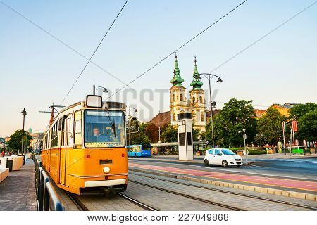 Budapest, Hungary. Yellow Tram Moving By The Embankment With St Anne Church. Morning View Of Budapes