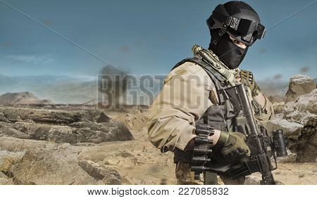 Photo of a fully equipped military soldier standing with rifle, ammo on desert battlefield background.