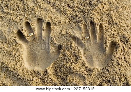 Two-handed Shape In The Sand With Wedding Rings On Ring Fingers. Feeling Of Union, Couple, Passion A
