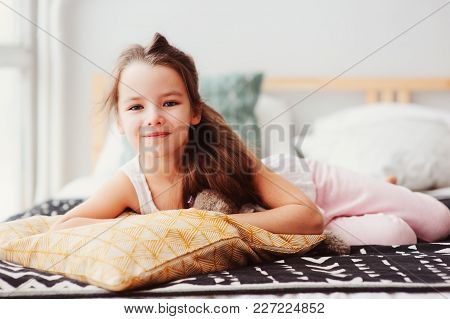 happy little child girl lying on her bed in the morning, waking up in comfortable room with modern b