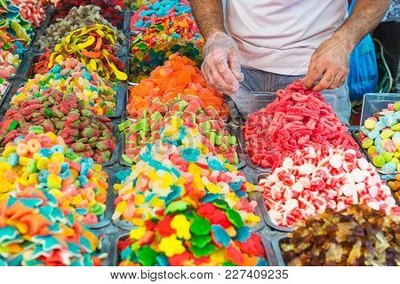 Seller Unfolds Sweets On Counter With Assorted Colorful Different Shape Jelly Candies On Market Plac