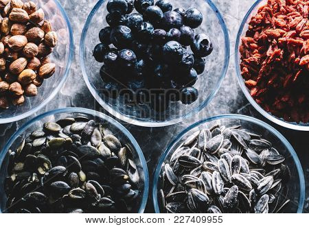 Five glass bowls of different superfoods. Brasilian nuts and almonds, blueberries, goji berries, pumpkin and sunflower seeds.