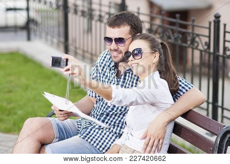 Traveling  Concepts. Young Caucasian Couple In Love Sitting On Bench Outdoors While Taking Selfie Pi