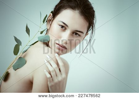 Beauty portrait. Sensual brunette girl with a green spring plant. Beauty, natural cosmetics concept.