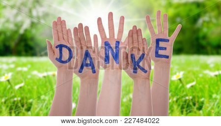 German Word Danke Means Thank You On Hands Of White Caucasian People. Sunny Grass Meadow In Backgrou
