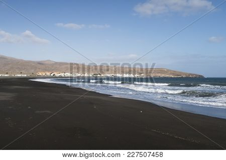Dark Sand Beach Near Tarajalejo On Fuerteventura Island Against Blue Sky