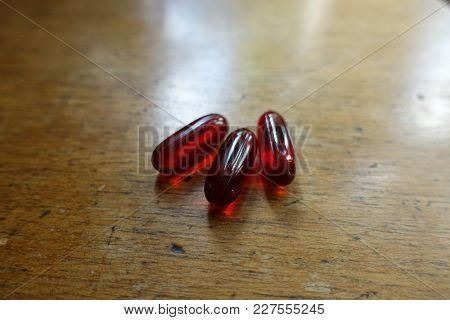 Three Red Capsules Of Krill Oil On Wood