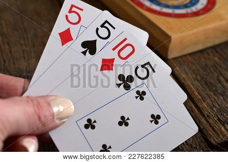A Close Up Image Of An Old Wooden Cribbage Board With Playing Cards.
