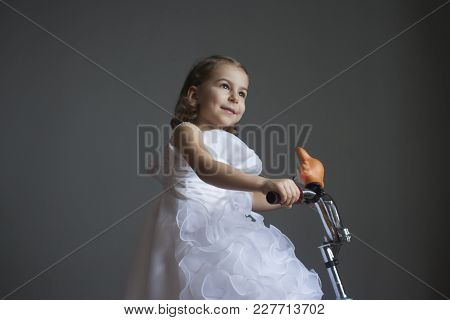 Little Girl In A Smart White Dress On A Bicycle