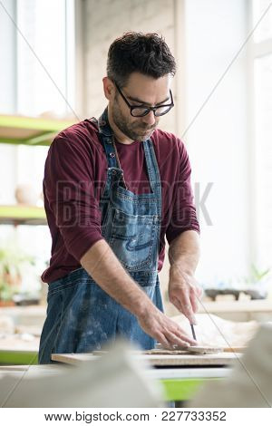 Ceramist Dressed in an Apron Cutting the Pieces of Raw Clay in the Bright Ceramic Workshop.
