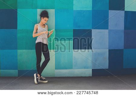 Happy Smiling African-american Woman Leaning On Bright Blue Graffiti Wall, While Listening Music, Re
