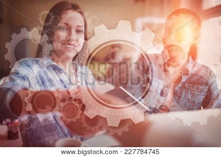White wheels and cogs on blue against businesswomen shaking hands in creative office